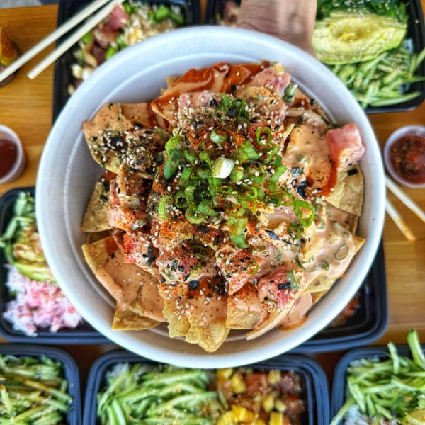 Tiger Plate poke nachos with spicy sauce, green onions, and sesame seeds, surrounded by other poke bowls.