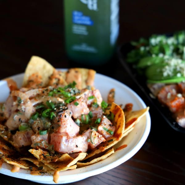 Tiger Plate's poke nachos, topped with sauce, sesame seeds, and green onions, with a drink in the background.