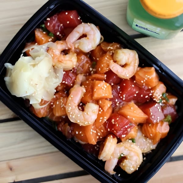 Tiger Plate's poke bowl with tuna, salmon, shrimp, and pickled ginger, on a wooden table.