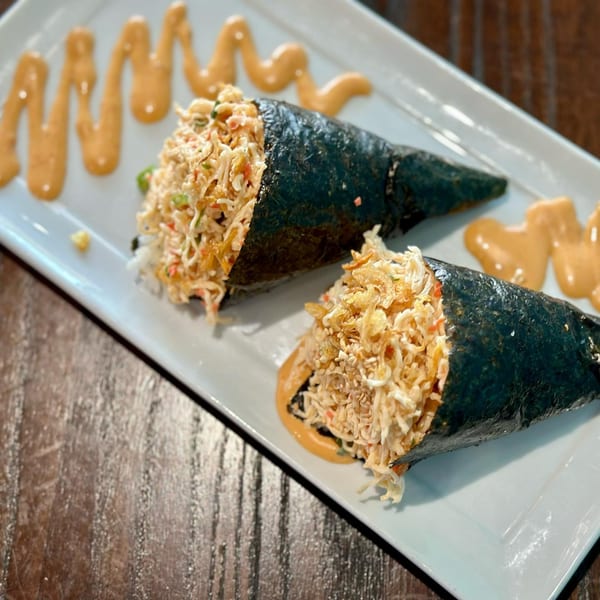 Two Tiger Plate poke hand rolls, filled with crab and crispy toppings, on a white plate with sauce.